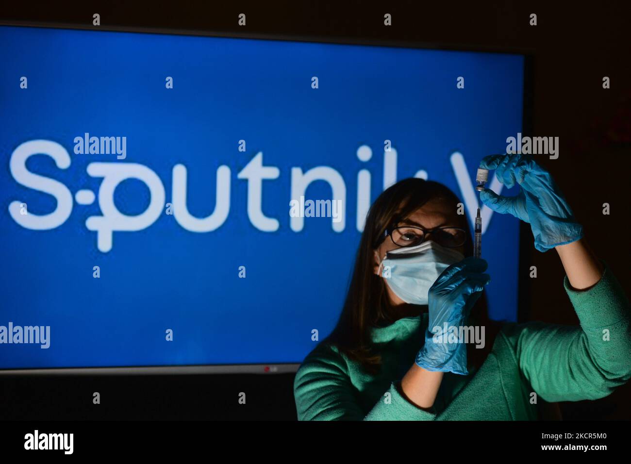 An illustrative image of a person holding a medical syringe and a vaccine vial in front of the Sputnik V logo displayed on a screen. On Thursday, October 21, 2021, in Edmonton, Alberta, Canada. (Photo by Artur Widak/NurPhoto) Stock Photo