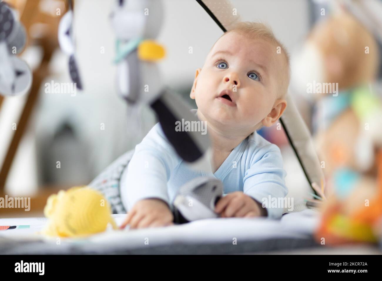 Cute baby boy playing with hanging toys arch on mat at home Baby activity and play center for early infant development. Baby playing at home. Stock Photo