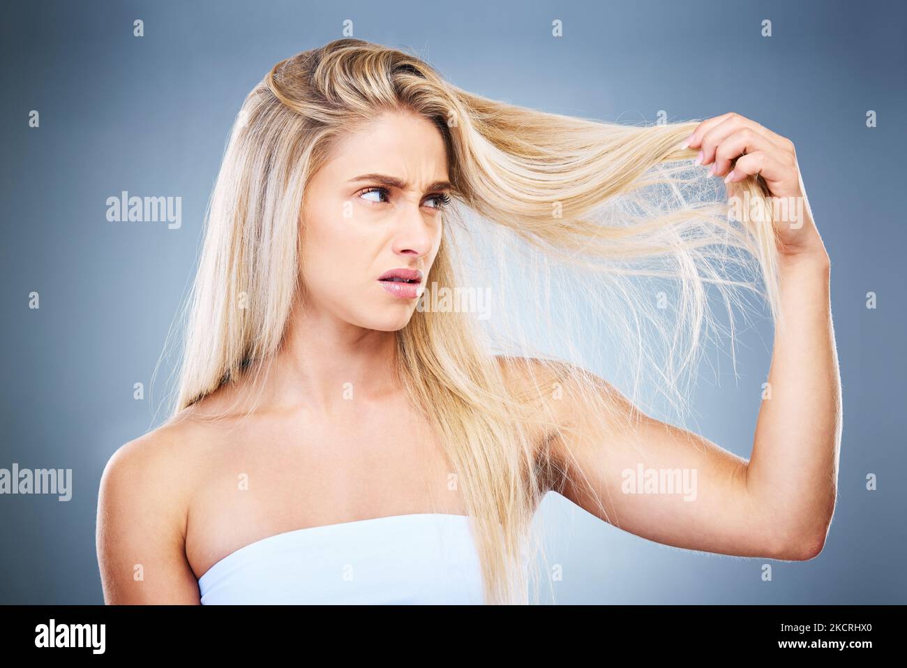 Upset, angry and annoyed woman with hair problem or style issue on a grey studio background. Damage, bad and expression of female unhappy with blonde Stock Photo