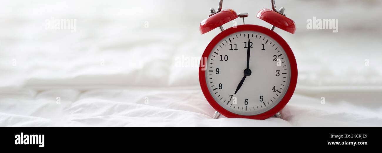 Red alarm clock at 7 oclock on bed Stock Photo Alamy