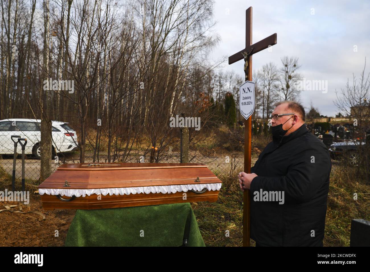 A worker of a burial service holds a crucifix with NN plate by a coffin of an unknown man, probably a migrant, who was found dead in a forest on September 19th by Polish-Belarusian border. Sokolka, Poland on November 22, 2021. A man was buried at the catholic cemetery but a priest did not conduct funeral rites as there was no evidence of what was the denomination of the deceased, despite a Holy Bible was found by the body. (Photo by Beata Zawrzel/NurPhoto) Stock Photo