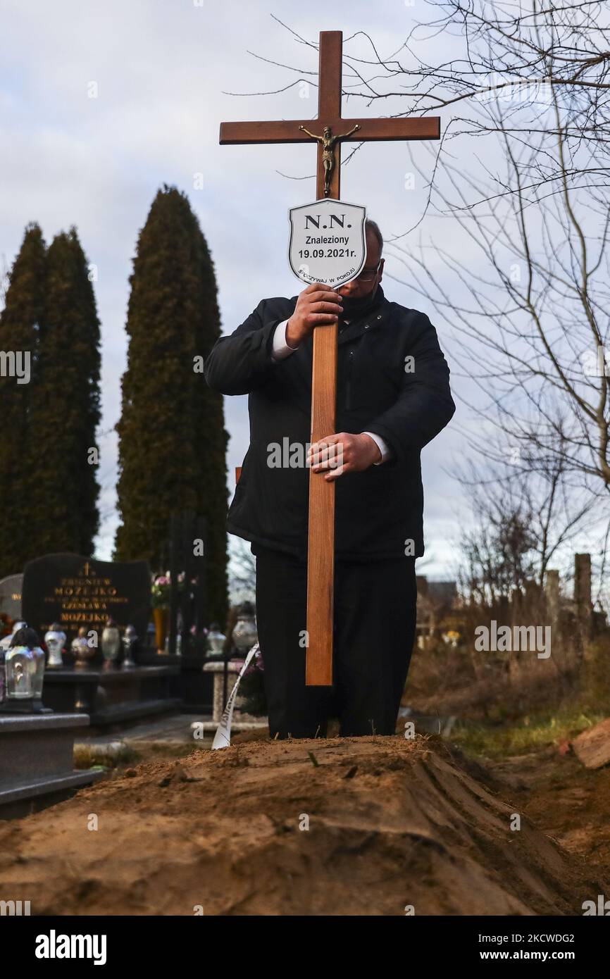 A worker of a burial service puts a crucifix with NN plate on a grave of an unknown man, probably a migrant, who was found dead in a forest on September 19th by Polish-Belarusian border. Sokolka, Poland on November 22, 2021. A man was buried at the catholic cemetery but a priest did not conduct funeral rites as there was no evidence of what was the denomination of the deceased, despite a Holy Bible was found by the body. (Photo by Beata Zawrzel/NurPhoto) Stock Photo
