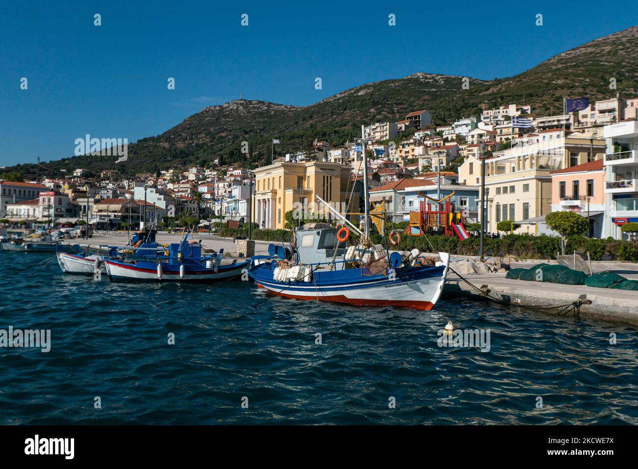 Beautiful traditional wooden fishing boats docked at the harbor of Samos town during a day with sun and blue sky. Samos town, Katho Vathi is a natural sea harbor, the port town and capital of Samos Island and regional unit known also as Vathy, the old name. Samos town was built in the middle of the 18th century as the port of Vathy and has a population of 8100 residents. In ancient times, Samos was an especially rich and powerful city-state, known for its vineyards and wine production while nowadays the Samian economy relies on the agriculture and tourist industry. Samos is the birthplace of t Stock Photo