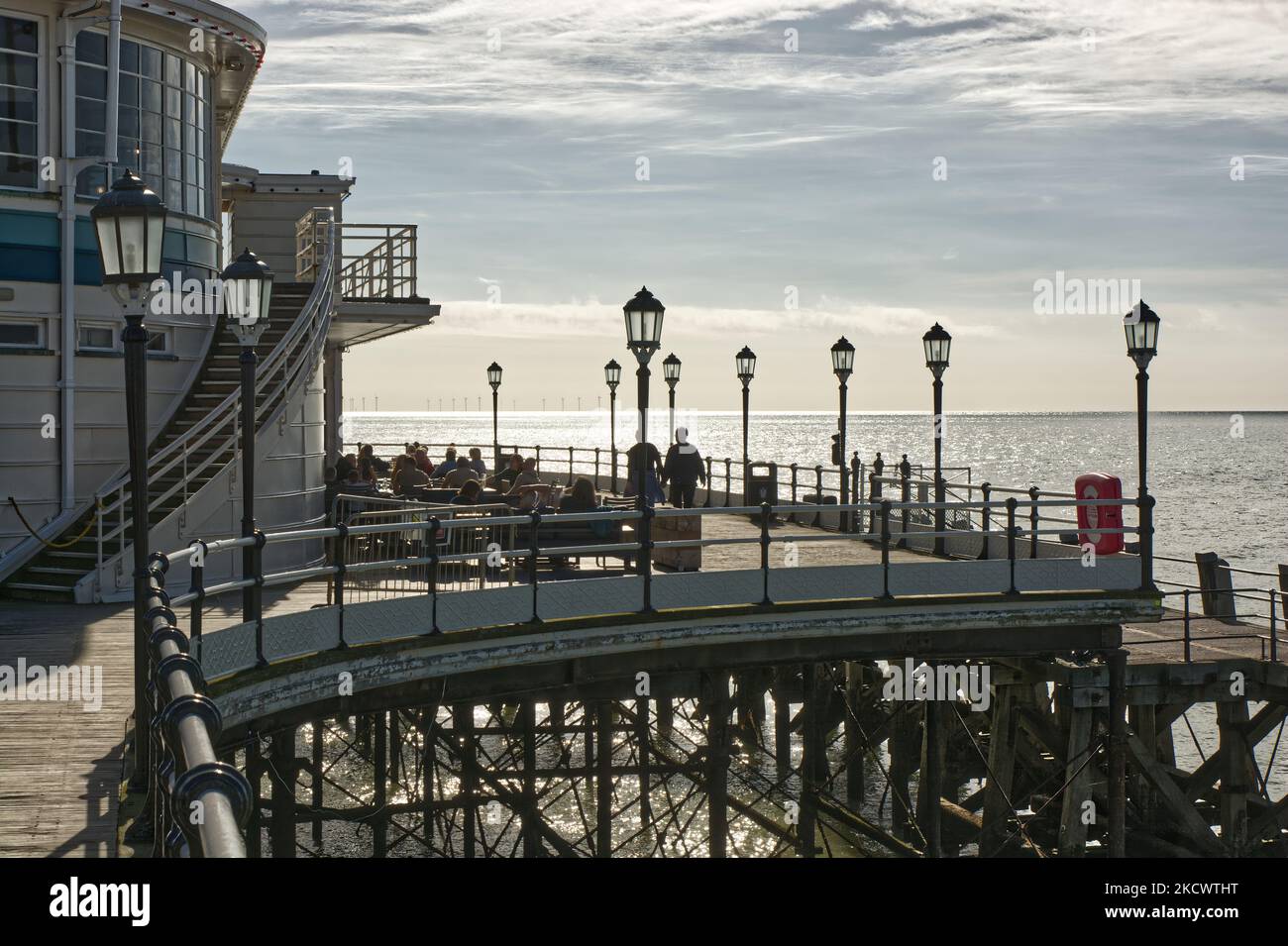 People sitting at cafe and restaurant terrace tables on the end of the pier at Worthing in West Sussex, England. With windfarm in far distance. Stock Photo
