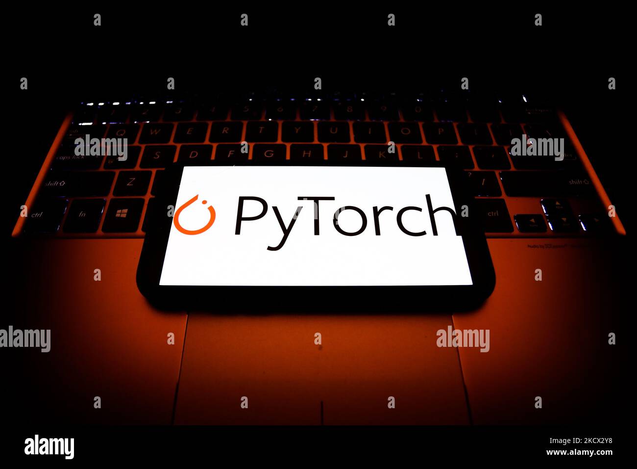 PyTorch logo displayed on a phone screen and a laptop keyboard are seen in this illustration photo taken in Krakow, Poland on December 1, 2021. (Photo by Jakub Porzycki/NurPhoto) Stock Photo