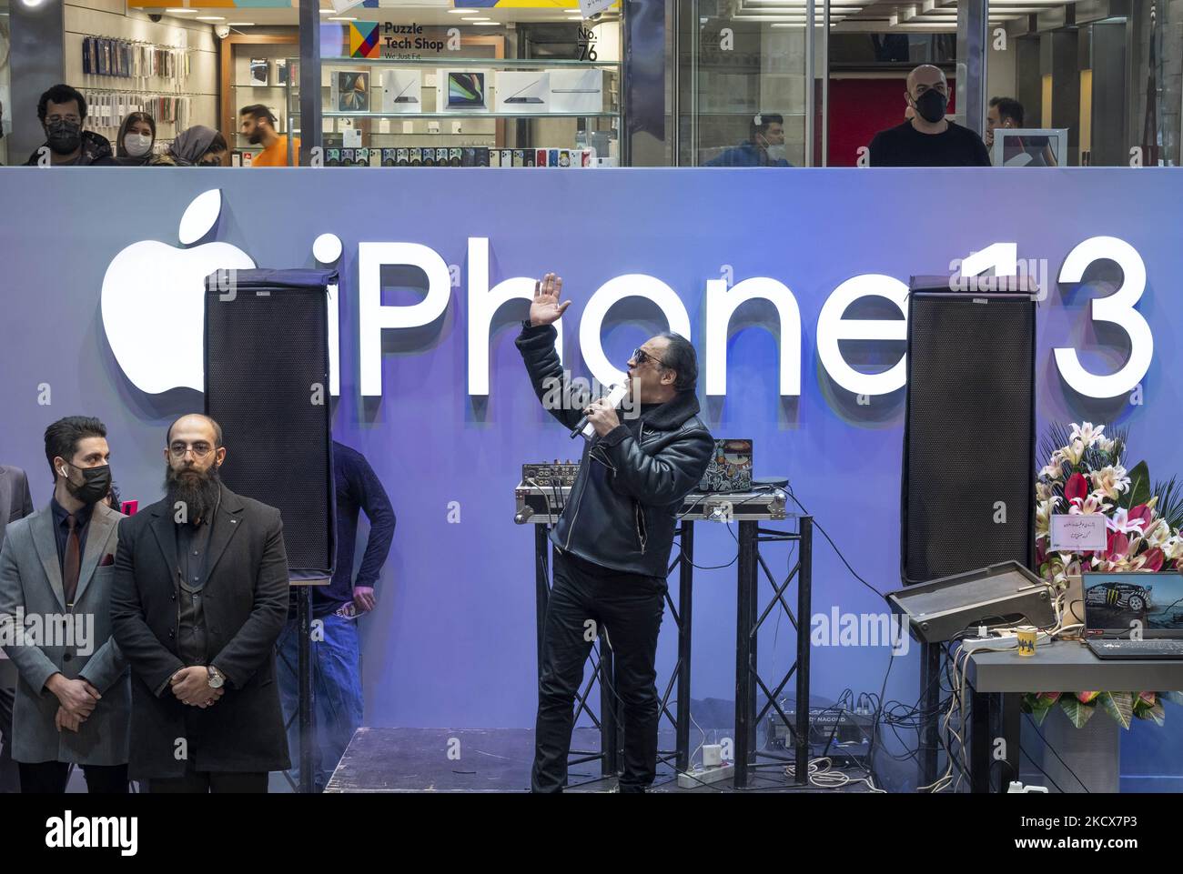 An Iranian showman (C) performs in front of a logo of the Apple American company’s iPhone 13 during an opening ceremony of the IT-City multi brand shop at the Paytakht computer centre in northern Tehran on December 1, 2021. Despite US sanctions against Iran, Iranians have access to the latest technology in the world of telecommunications and digital, but in most cases at a higher price than the global value of technology goods, but the Iranians prefer to keep themselves update themselves in the field of the computers and telecommunication technology. Even though they have to have to get loan t Stock Photo