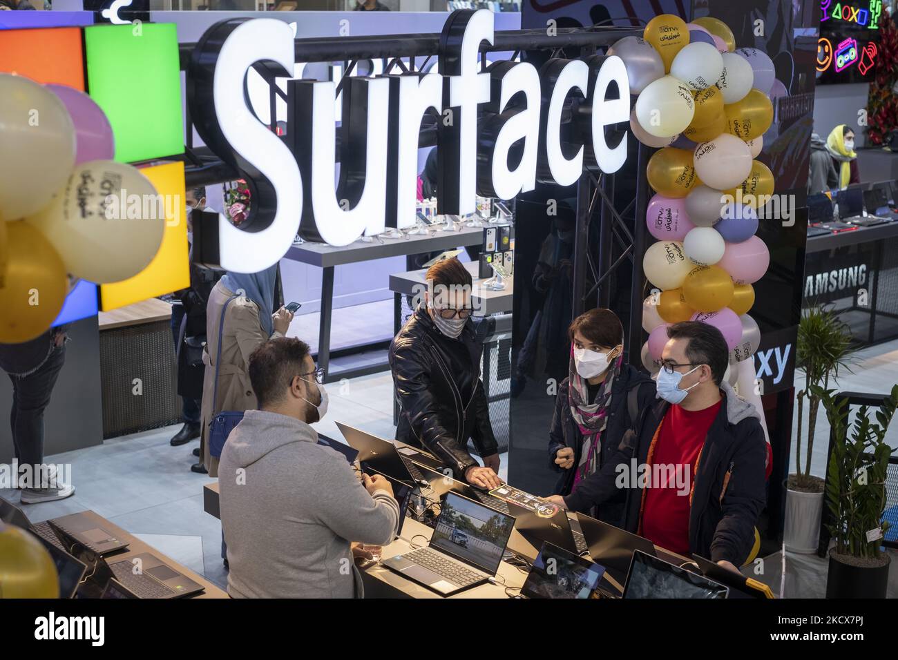 An Iranian salesman (L) speaks with his clients as they stand under a logo of the Microsoft American company in an IT-City multi brand shop at the Paytakht computer centre in northern Tehran on December 2, 2021. Despite US sanctions against Iran, Iranians have access to the latest technology in the world of telecommunications and digital, but in most cases at a higher price than the global value of technology goods, but the Iranians prefer to keep themselves update themselves in the field of the computers and telecommunication technology. Even though they have to have to get loan to buy a new  Stock Photo