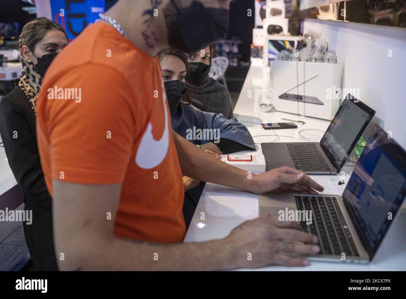 An Iranian salesman checks a smartphone’s serial number on a laptop for his clients in an IT-City multi brand shop at the Paytakht computer centre in northern Tehran on December 2, 2021. Despite US sanctions against Iran, Iranians have access to the latest technology in the world of telecommunications and digital, but in most cases at a higher price than the global value of technology goods, but the Iranians prefer to keep themselves update themselves in the field of the computers and telecommunication technology. Even though they have to have to get loan to buy a new smartphone like the iPhon Stock Photo