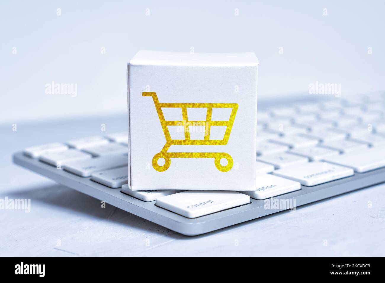 Tiny white cardboard shipping box with a golden shopping cart marking placed on a new keyboard. Stock Photo