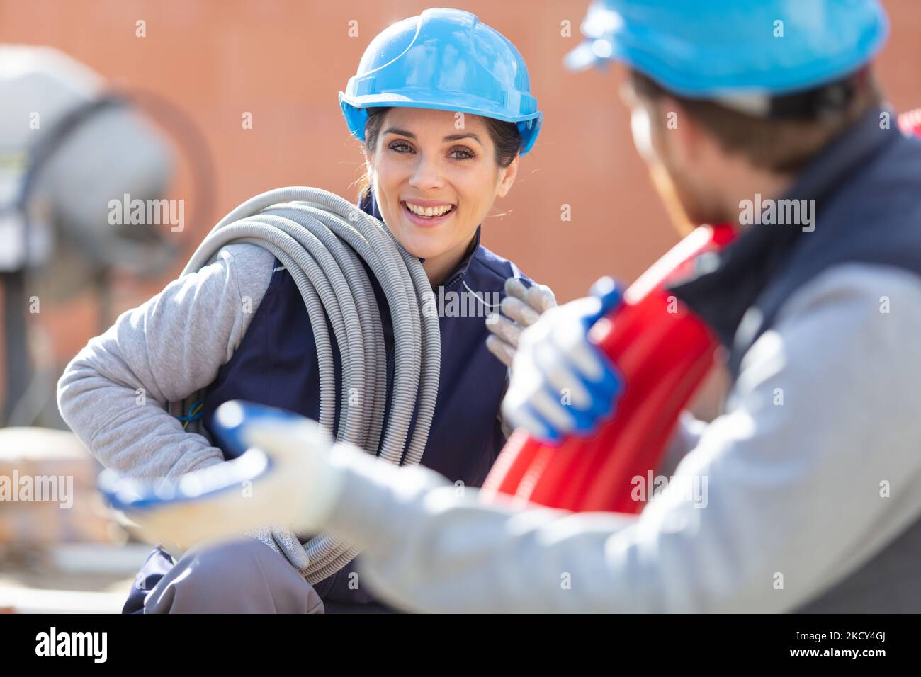 female labourer with reel of pipe over shoulder Stock Photo