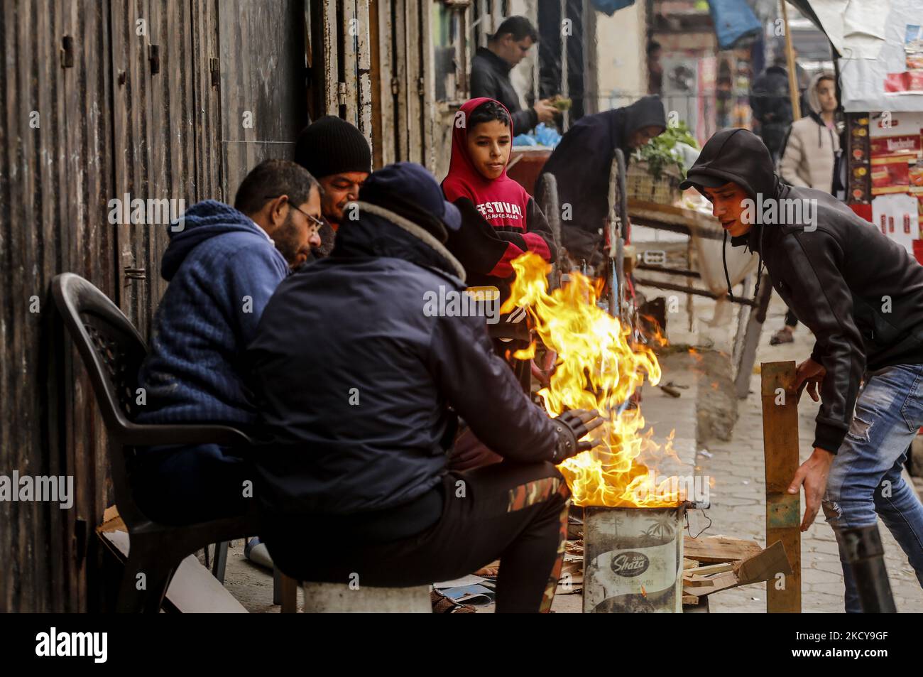 Palestinian refugees sit around the fire outside their home to warm ...