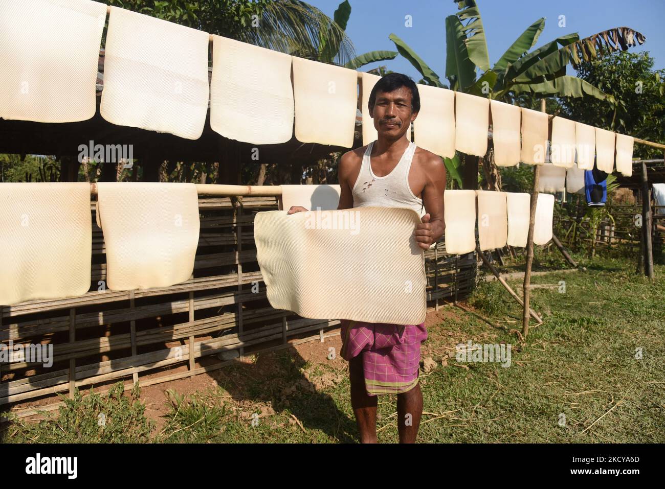 A person holding up a rubber sheet, one of many that are hanged to dry, in a village on December