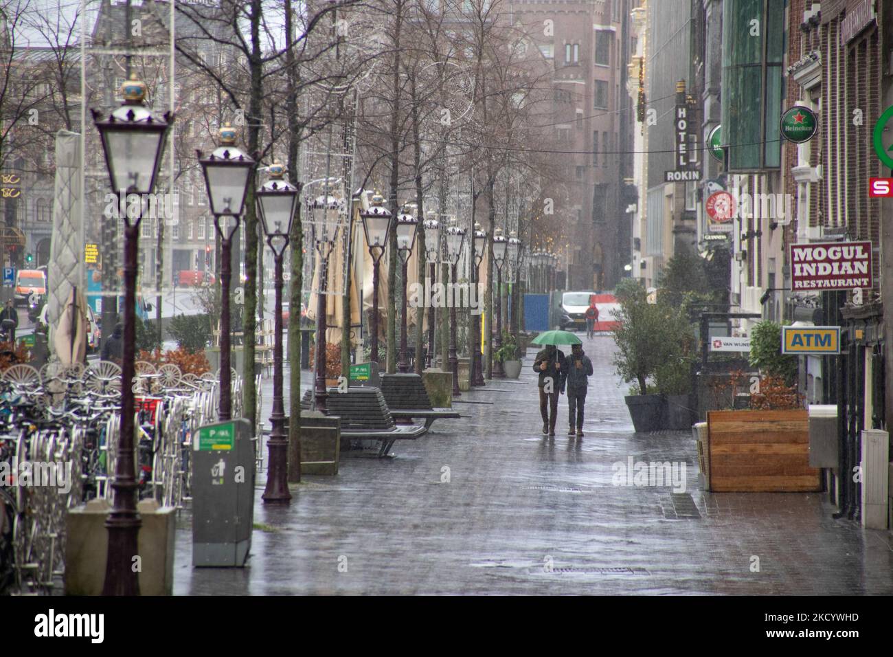 Quiet, almost deserted from local people and tourists streets of Amsterdam during the lockdown in the Dutch capital city with stores and shops appearing with closed with the roller metal shutter down, cafes, bars and restaurants also closed with tables and chairs of the terraces locked. The Netherlands was the first European nation to declare full lockdown to fight the new Omicron variant that surges. After a sudden government order before Christmas, the country closed all the nonessential shops, cafes, restaurants, bars, gyms, schools, sports venues, cultural places and others for 4 weeks in  Stock Photo