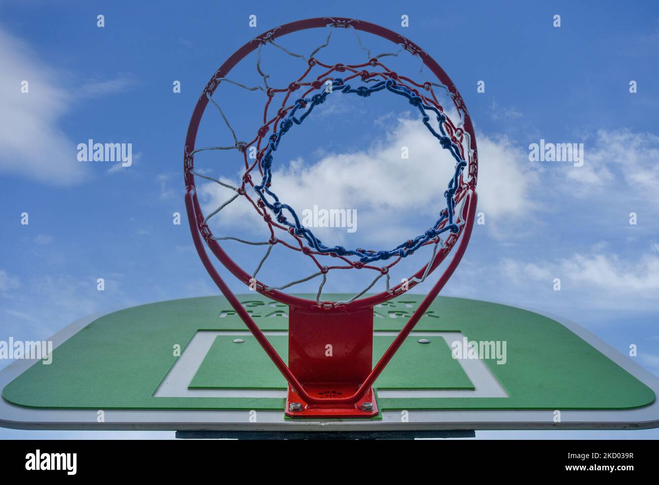 Looking skywards through a basketball hoop towards a blue sky with white clouds. Stock Photo