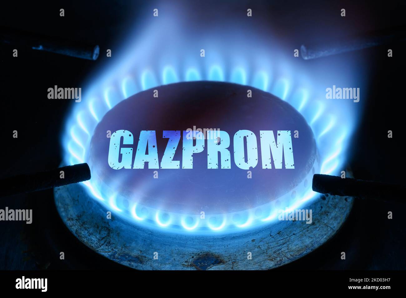Gas burns in dark at home, blue fire flame and name Gazprom on stove ring burner. Concept of natural pipeline gas cost, warmth, energy crisis, economy Stock Photo