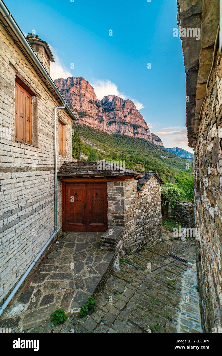 View of the beautiful picturesque traditional Greek village Mikro Papigo translated as Little Papingo, with the famous stone building architecture of the house, roads and church in high altitude under the Astraka Towers mountain peak in Zagori area, near the Vikos Canyon in Epirus during the fall. The village is in Vikos–Aoös National Park that is part of the Natura 2000 ecological network and a UNESCO Geopark making it a travel destination for tourists. People visit the village to enjoy activities including rafting, canoe-kayaking, hiking and mountain biking, the gastronomy of the area and th Stock Photo