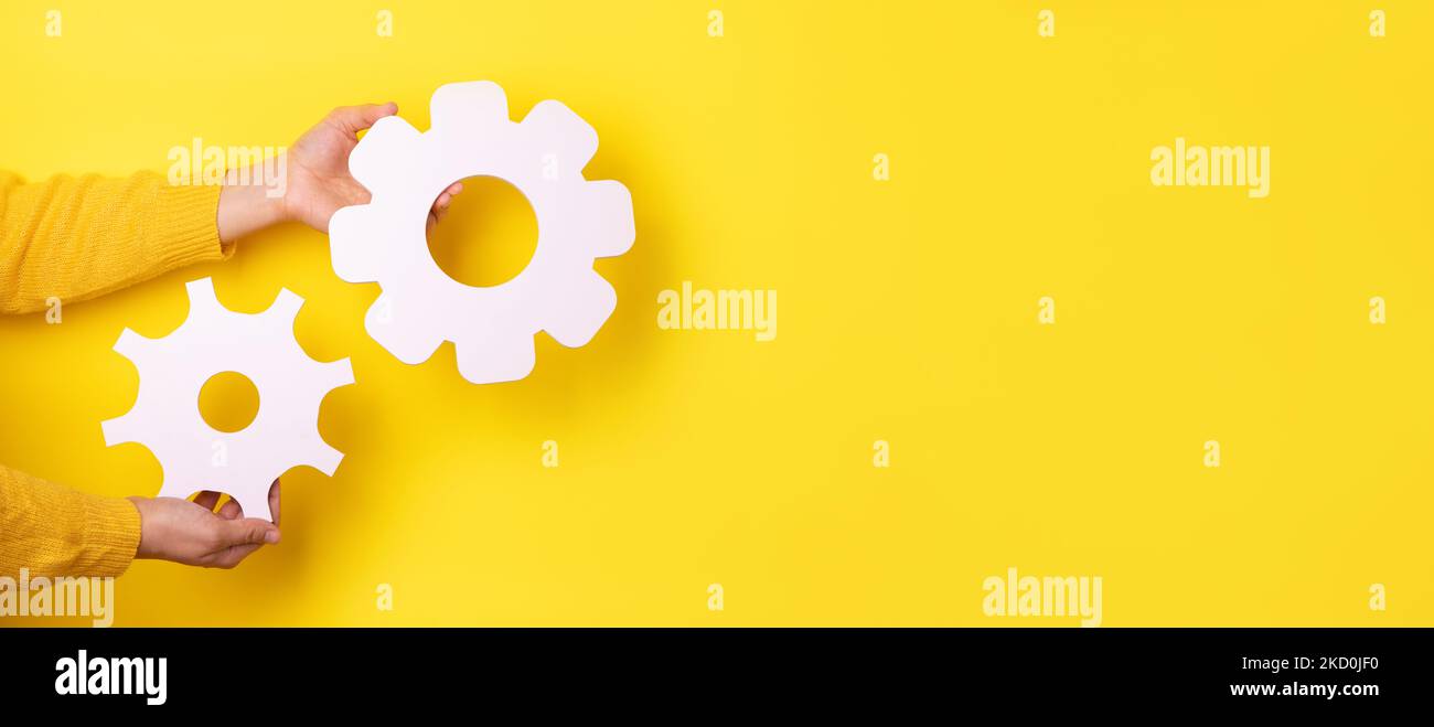 gear symbol in hands over yellow background, panoramic layout Stock Photo