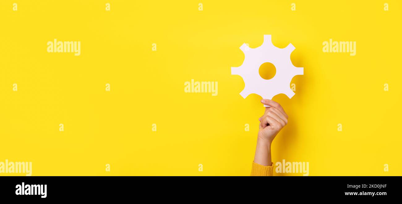 hand holding gear symbol over yellow background, panoramic layout Stock Photo