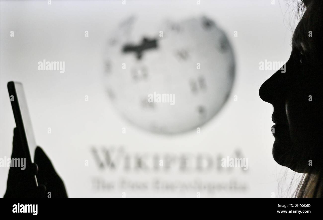An image of a woman holding a cell phone in front of the Wikipedia logo displayed on a computer screen. On Tuesday, January 12, 2021, in Edmonton, Alberta, Canada. (Photo by Artur Widak/NurPhoto) Stock Photo