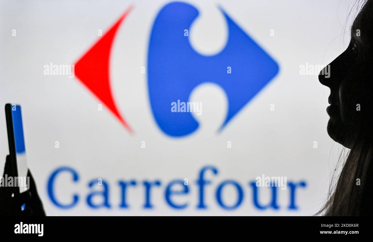 An image of a woman holding a cell phone in front of the Carrefour logo displayed on a computer screen. On Tuesday, January 12, 2021, in Edmonton, Alberta, Canada. (Photo by Artur Widak/NurPhoto) Stock Photo