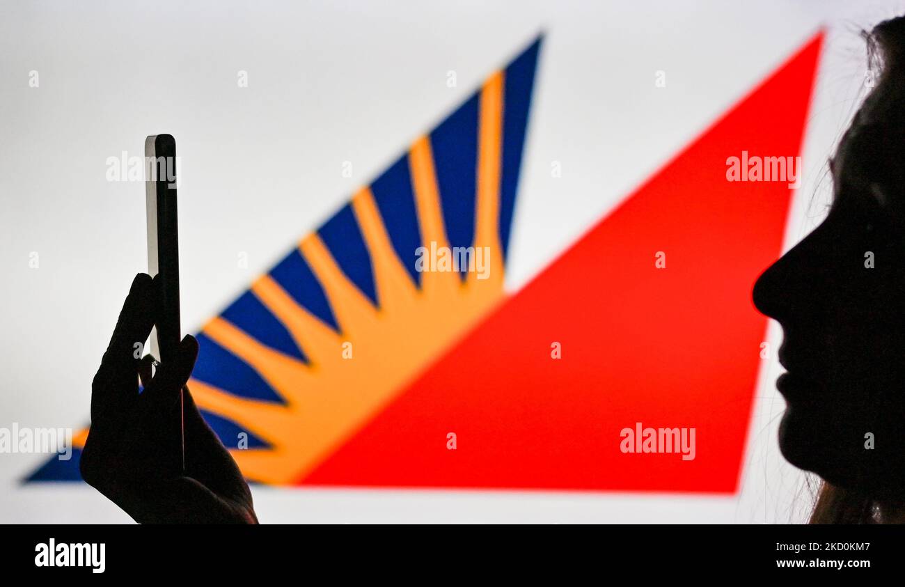 An image of a woman holding a cell phone in front of the Philippine Airlines logo displayed on a computer screen. On Tuesday, January 12, 2021, in Edmonton, Alberta, Canada. (Photo by Artur Widak/NurPhoto) Stock Photo