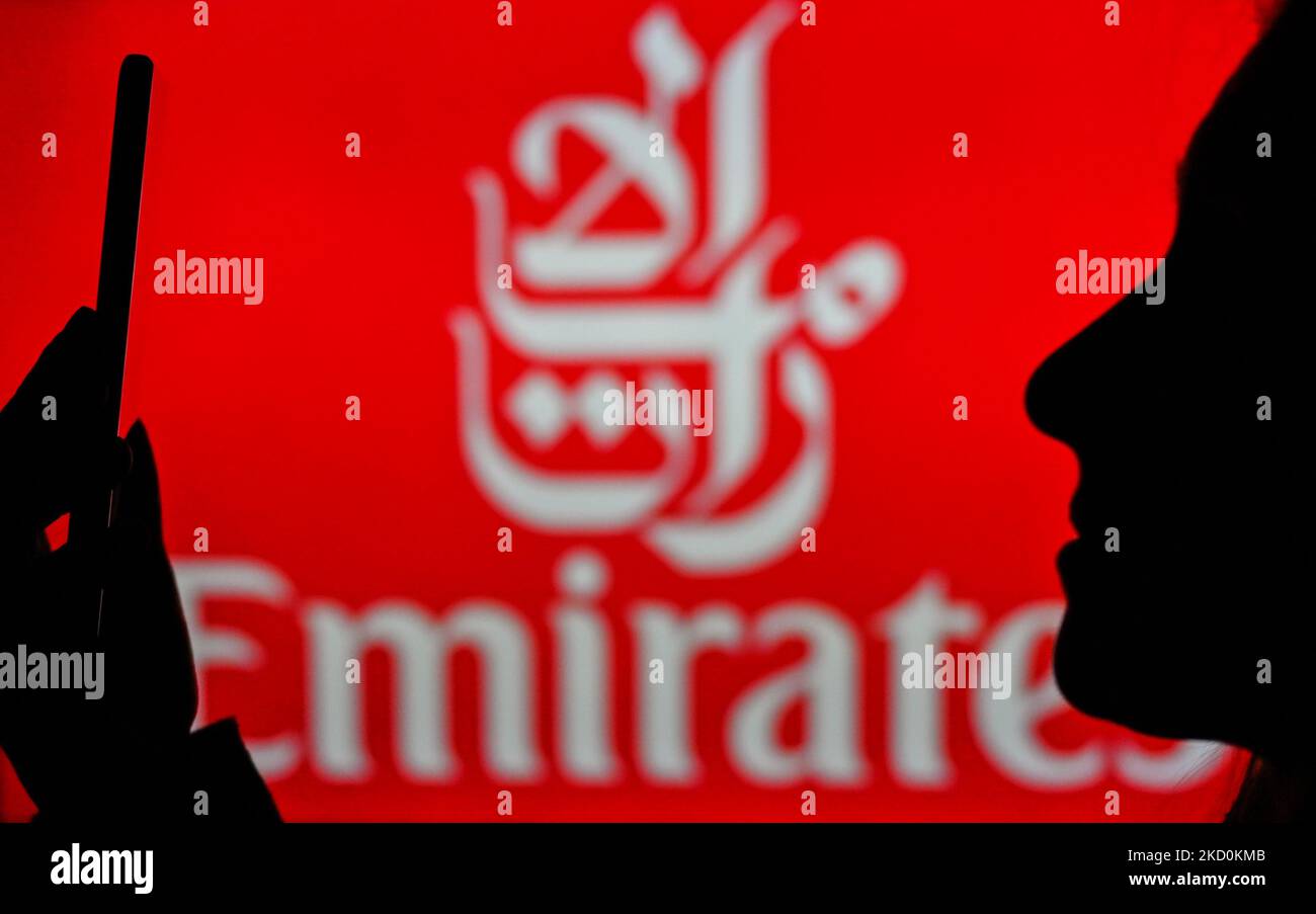 An image of a woman holding a cell phone in front of the Emirates logo displayed on a computer screen. On Tuesday, January 12, 2021, in Edmonton, Alberta, Canada. (Photo by Artur Widak/NurPhoto) Stock Photo