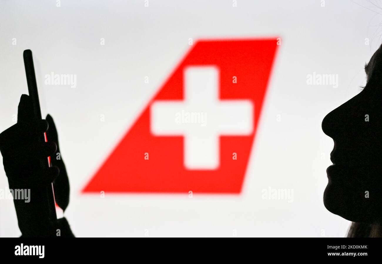 An image of a woman holding a cell phone in front of the Swiss International Air Lines logo displayed on a computer screen. On Tuesday, January 12, 2021, in Edmonton, Alberta, Canada. (Photo by Artur Widak/NurPhoto) Stock Photo