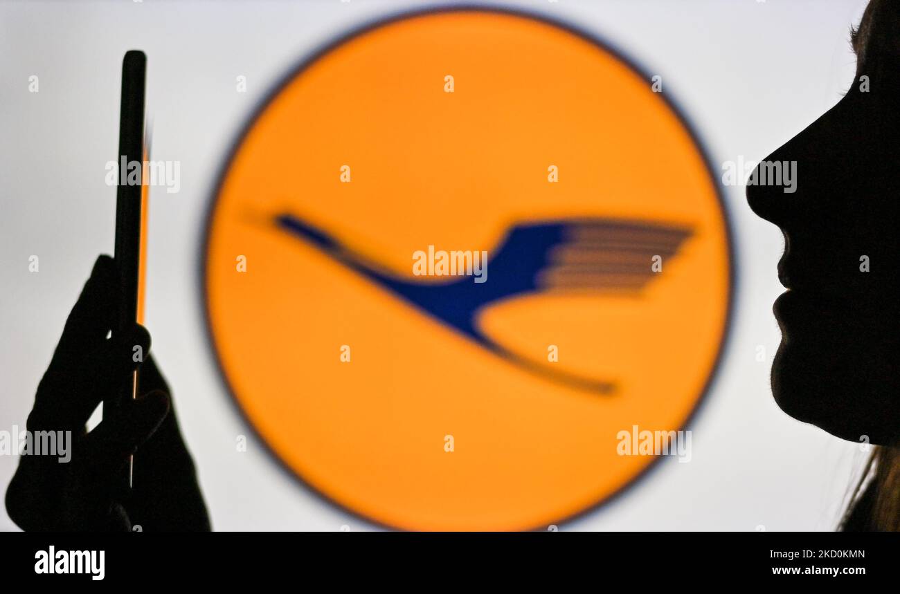 An image of a woman holding a cell phone in front of the Lufthansa logo displayed on a computer screen. On Tuesday, January 12, 2021, in Edmonton, Alberta, Canada. (Photo by Artur Widak/NurPhoto) Stock Photo