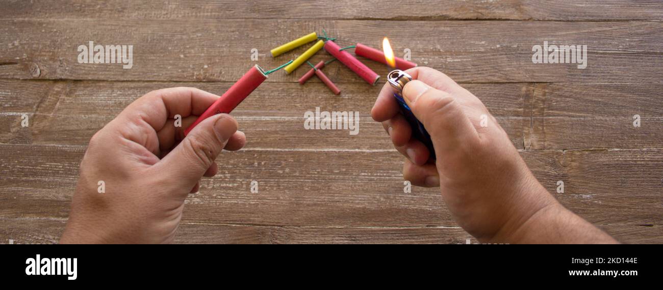 Image of the hands of a man who lights the fuse of a firecracker with a lighter. Reference you have celebrations and the danger of the barrels. Banner Stock Photo