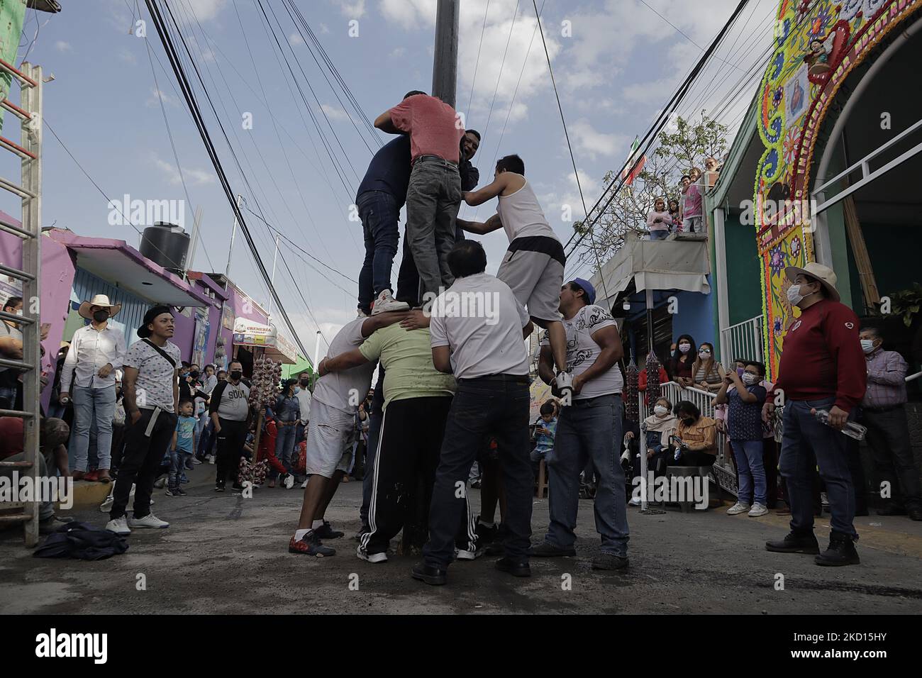 Several young people participate in the game called Palo Ensebado or Cucaña, played in the streets of San Antonio Culhuacán in Mexico City to celebrate the patron saint of animals, San Antonio Abad, which took place during the COVID-19 health emergency and the return to the yellow epidemiological traffic light after the increase in coronavirus infections in the capital. This game originated in Naples, Italy, in the 16th century. In its Mexican version, it consists of organising a team of people of different complexions to obtain the prizes that are placed at the top of a stick smeared with lar Stock Photo
