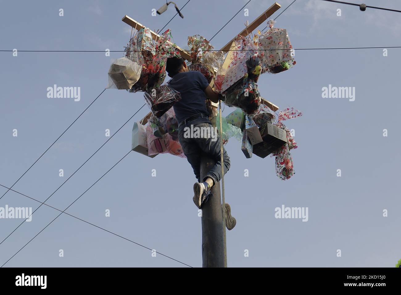 A young man reaches the top of a pole to obtain several prizes as the winner during the game called Palo Ensebado or Cucaña, held in the streets of San Antonio Culhuacán in Mexico City on the occasion of the celebration of San Antonio Abad, patron saint of animals, which took place during the COVID-19 health emergency and the return to the yellow epidemiological traffic light after the increase in coronavirus infections in the capital. This game originated in Naples, Italy, in the 16th century. In its Mexican version, it consists of organising a team of people of different complexions to obtai Stock Photo