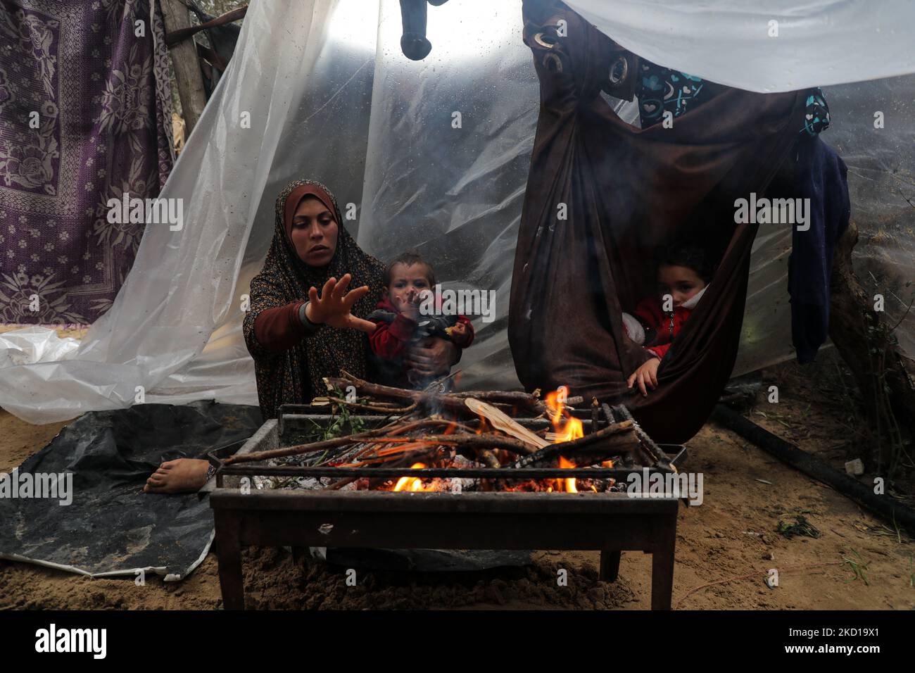 A Palestinian family keeps warm next to a fire during rainy and cold ...