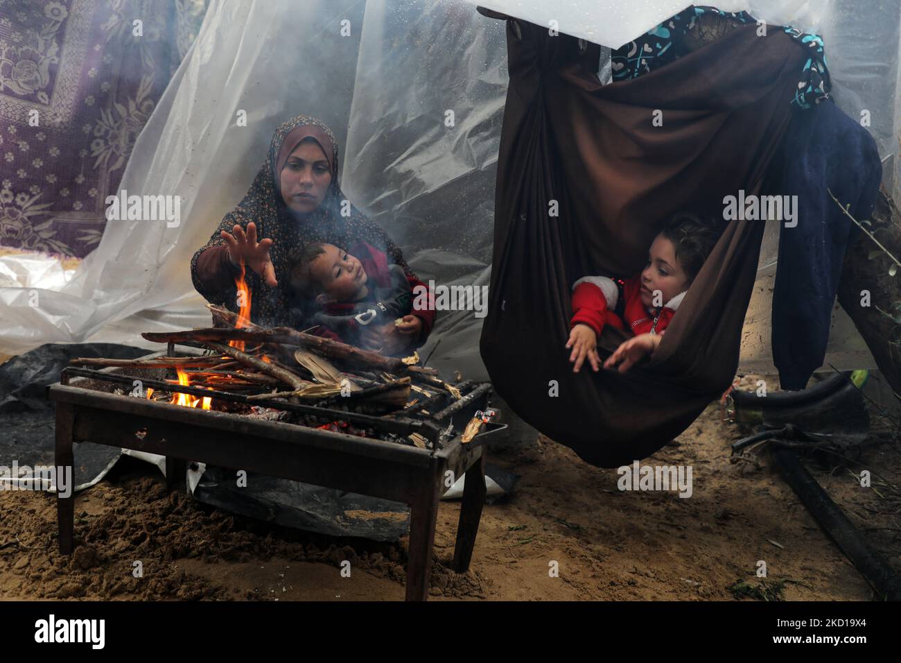 A Palestinian family keeps warm next to a fire during rainy and cold ...