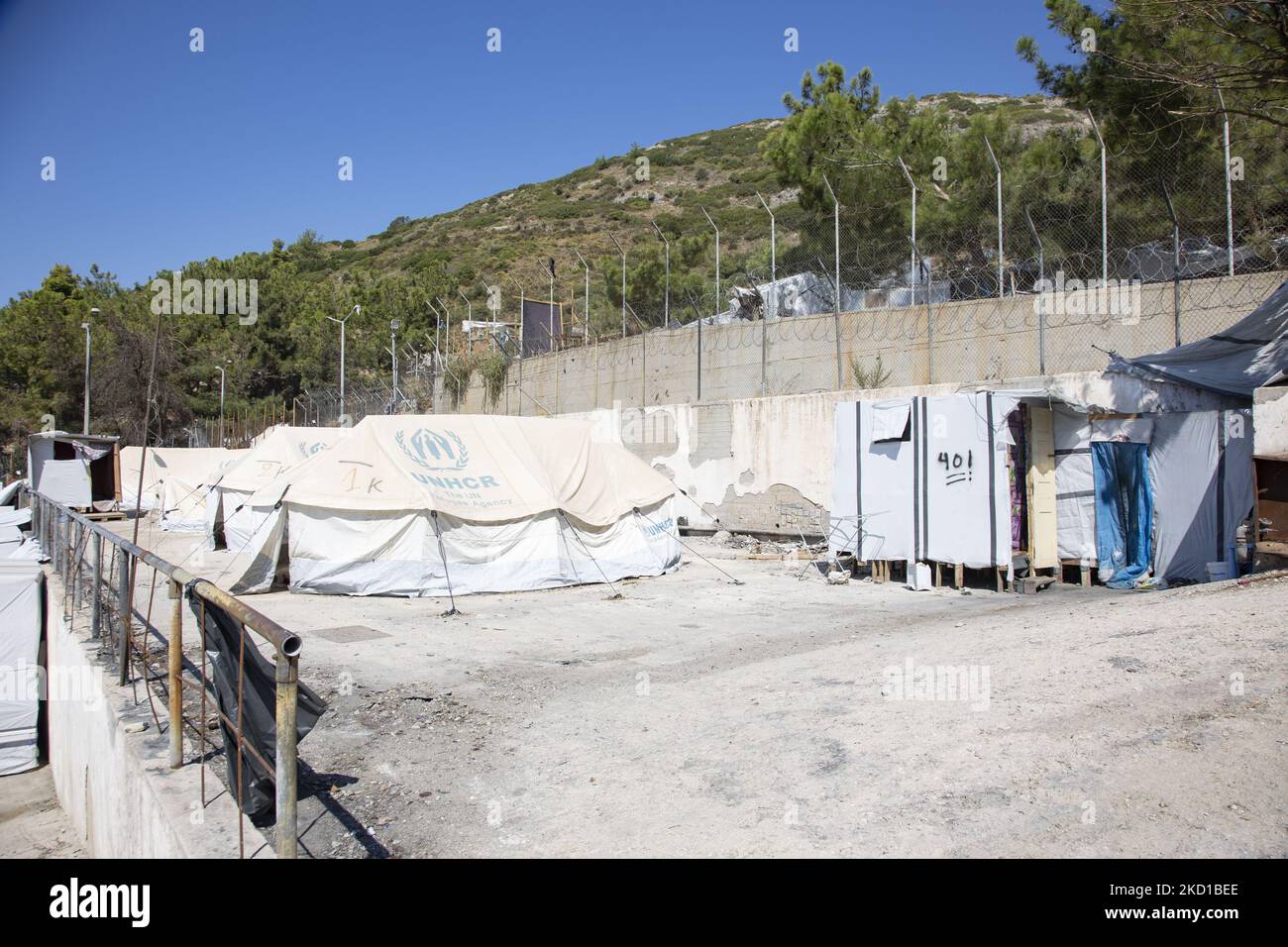 White tents in the official camp with the UNHCR - THE UN Refugee agency logo. The former official refugee - migrant camp surrounded by barbed wire fence at Vathy of Samos Island and the neighboring makeshift camp with handmade tents and some from UNHCR that is located just next to the houses of Vathi town, as seen deserted. The camp has been emptied and people relocated or moved with the police escort to the new camp and some very few houses. Once this facility hosted at its peak 7500 asylum seekers at the official facilities but also the makeshift camp in the forest that was nicknamed The Jun Stock Photo