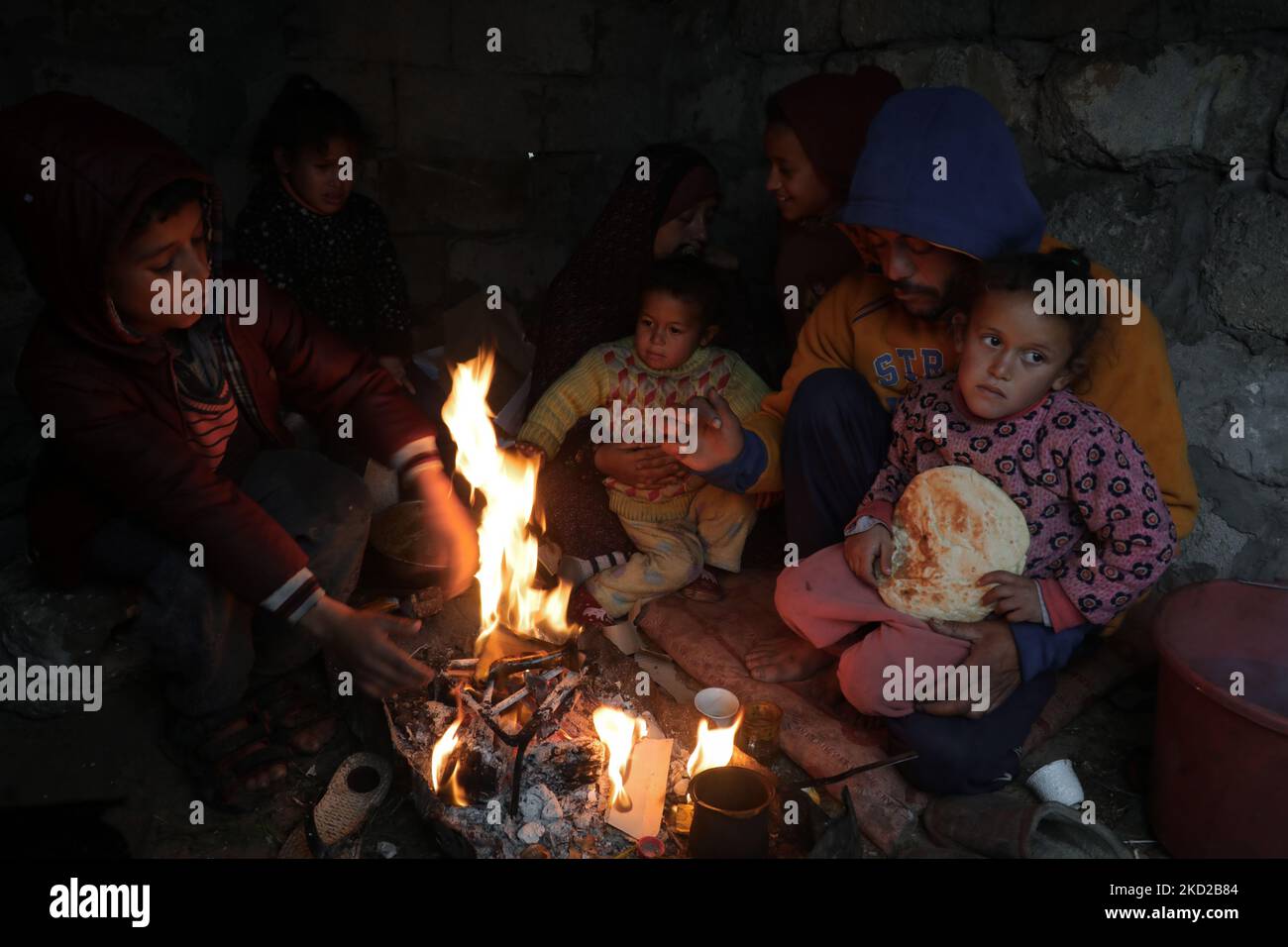 A Palestinian family keeps warm next to a fire on a rainy day in Khan ...