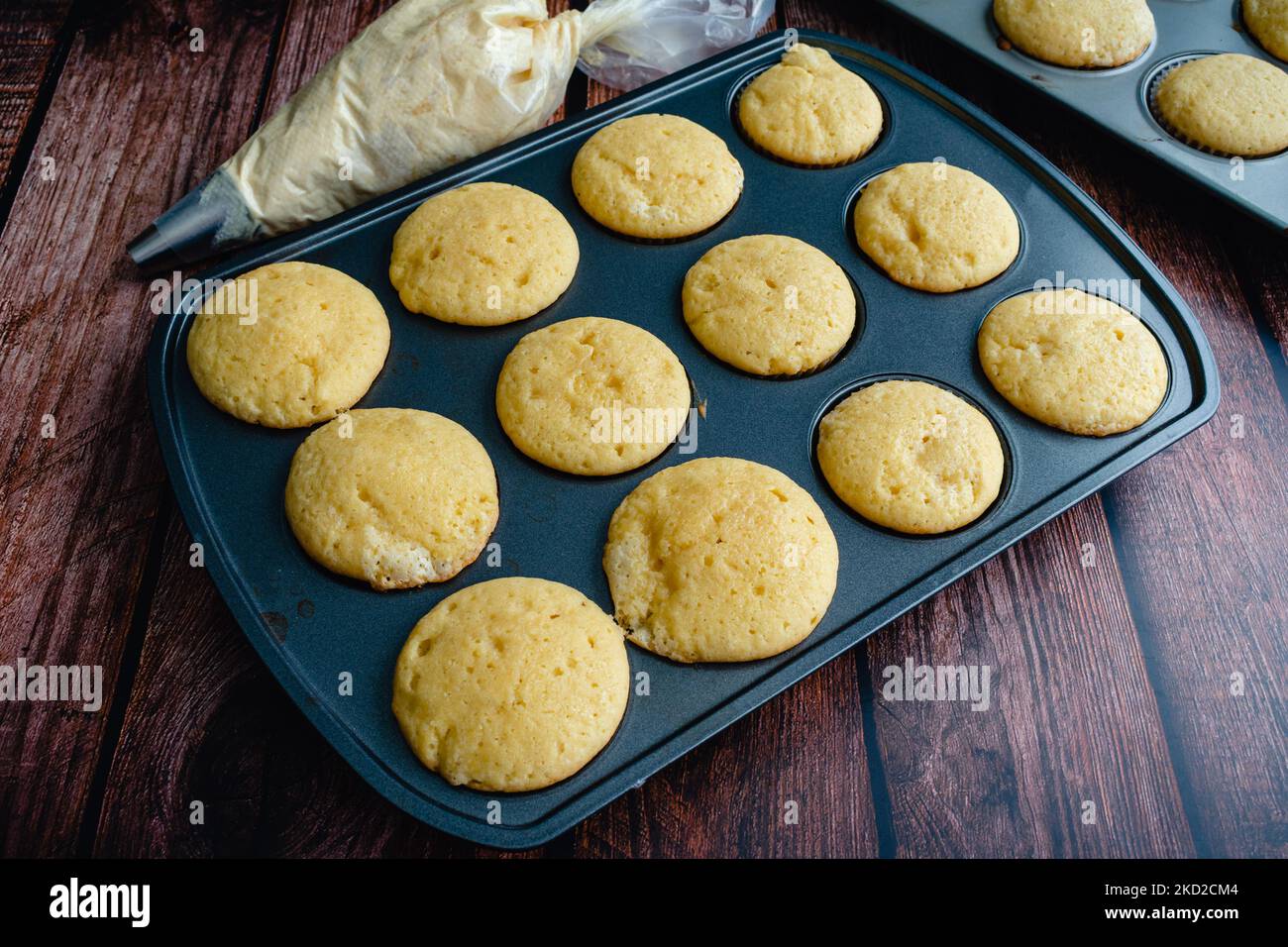 Vanilla Cupcakes in a Muffin Pan with a Piping Bag of Buttercream Vanilla cupcakes without
