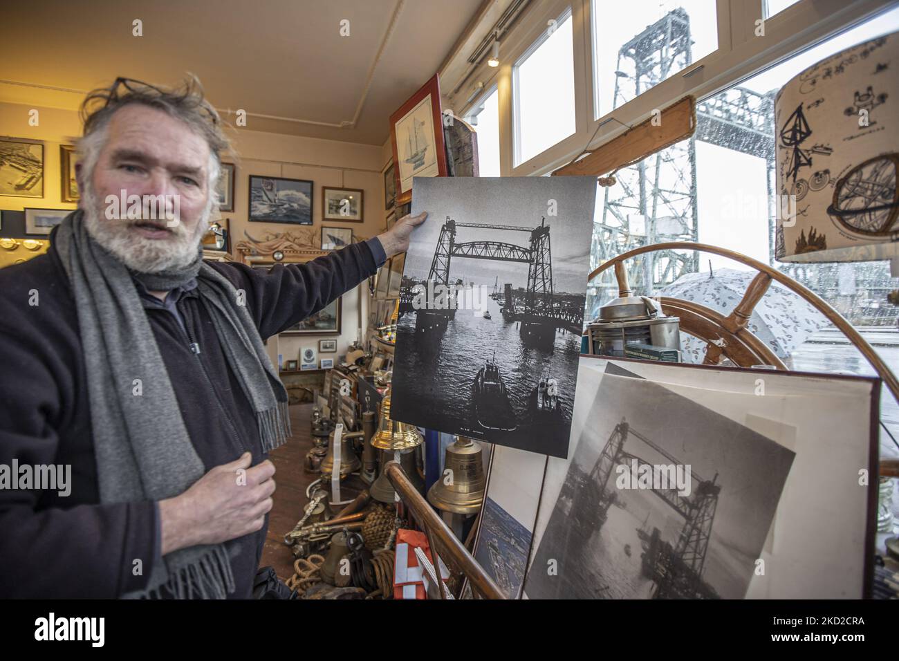 Shopkeeper of a Nautical store near the bridge Klaas Jan Hoeve is showing a historic old black and white picture of the bridge with the bridge been visible out. The iconic historic De Hef - Koningshavenbrug Bridge in the Dutch port city of Rotterdam may be dismantled for Jeff Bezos superyacht to pass under, as the mast of the sailboat exceeds the height of the bridge. The two-tower with swing lift bridge is an old level steel railroad bridge connecting the island, Noordereiland in the Maas river in the Southern part of Rotterdam. The bridge was built in 1877 and suffered damage during the 1940 Stock Photo