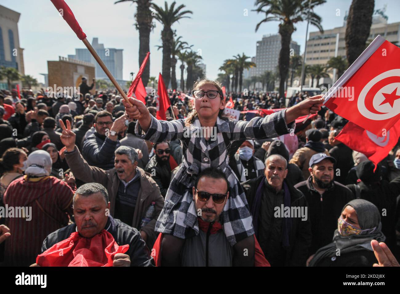 A young girl on a demonstrator’s shoulders, shouts slogans as she waves Tunisian flags during a demonstration held at the initiative of “Citizens Against the Coup - the Democratic Initiative” campaign, on Mohamed 5 avenue in the capital Tunis, Tunisia, on February 13, 2022, to protest against the dissolution of the country’s Supreme Judicial Council and called for the independence of the judiciary. Protesters also called for the release of the Vice President of Ennahda party, Noureddine Bhiri who is placed under house arrest since more than six weeks. Demonstrators also protested against what  Stock Photo