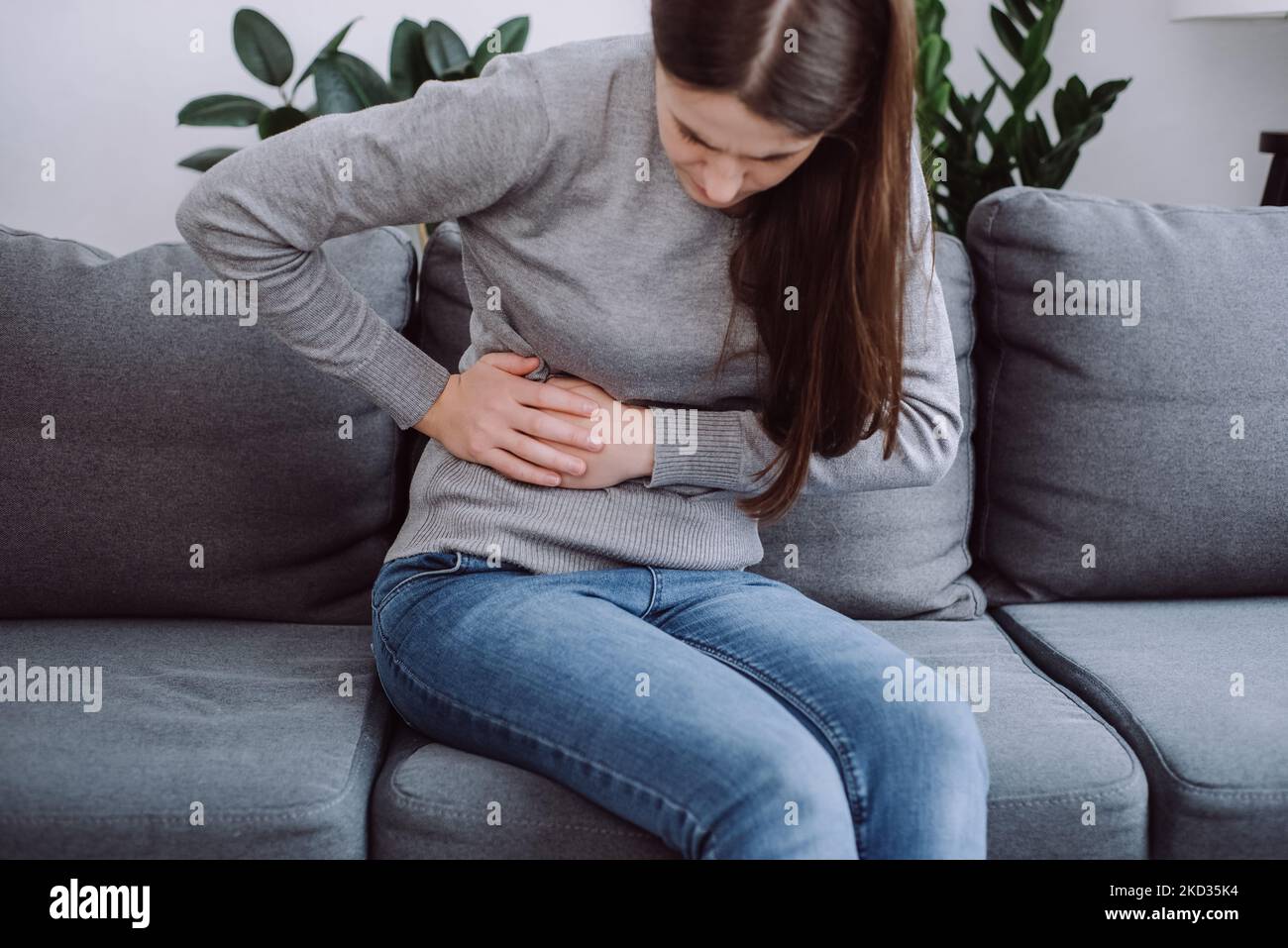 Selective focus of young woman holding hands in stomach ache, suffer from food poisoning, abdominal pain and colon problem, gastritis or diarrhoea. Pa Stock Photo