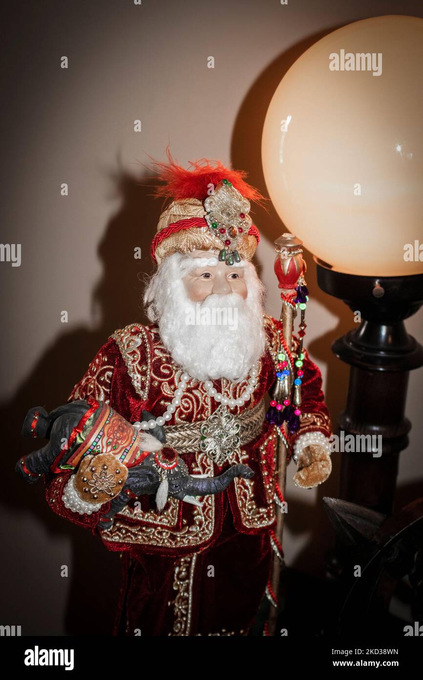 East Indian Santa figure holding little elephant with headress and jeweled stick standing by large retro globe lamp - Christmas decor Stock Photo