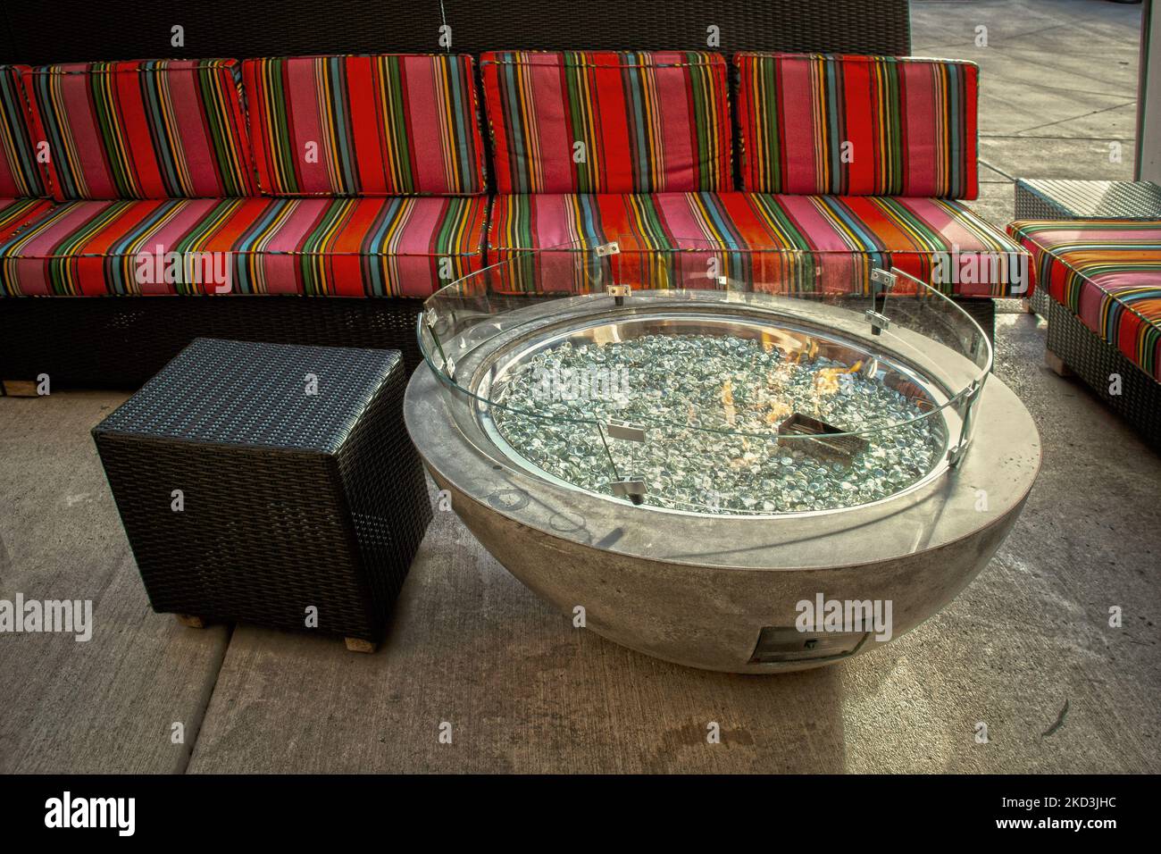 Firepit with glass pebbles in outdoor seating area with brightly striped and wiker furniture Stock Photo