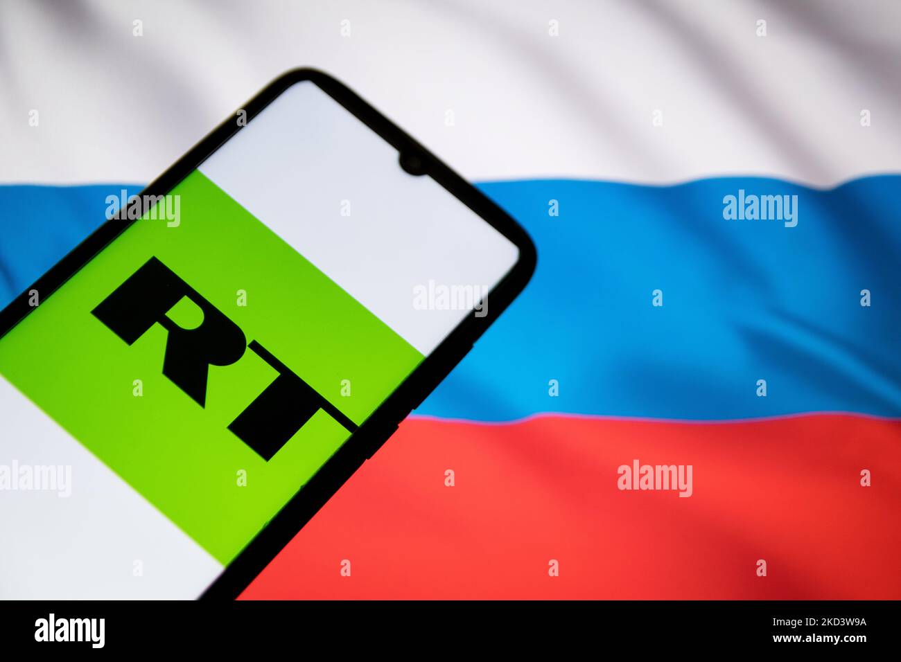 In this photo illustration a RT News logo seen displayed on a smartphone screen with a flag of Russia in the background in Athens, Greece on February 28, 2022. Google blocks Russia's RT News app downloads on Ukrainian territory. (Photo illustration by Nikolas Kokovlis/NurPhoto) Stock Photo
