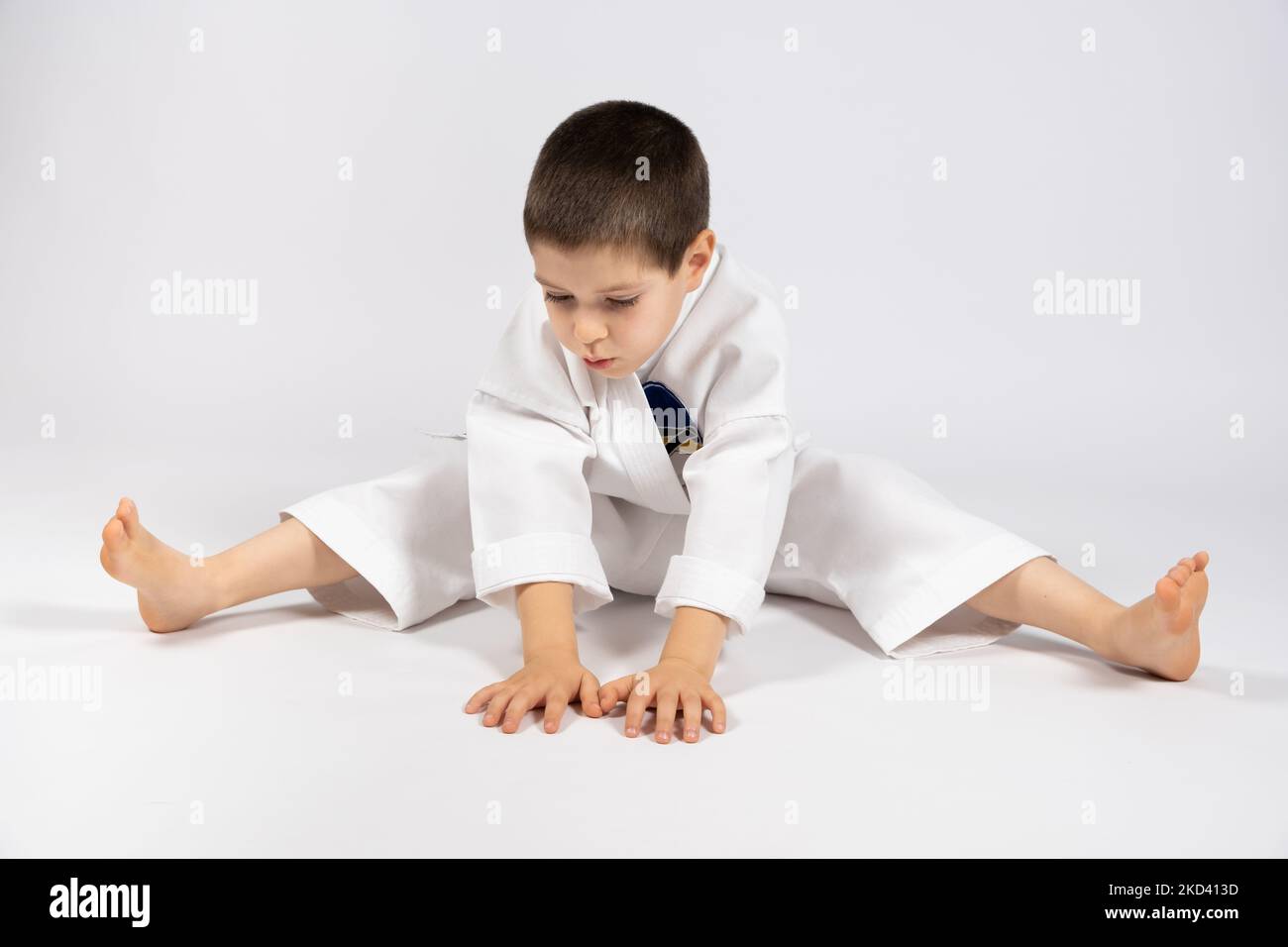 A 5yearold boy practices karate, stretches his legs on a white