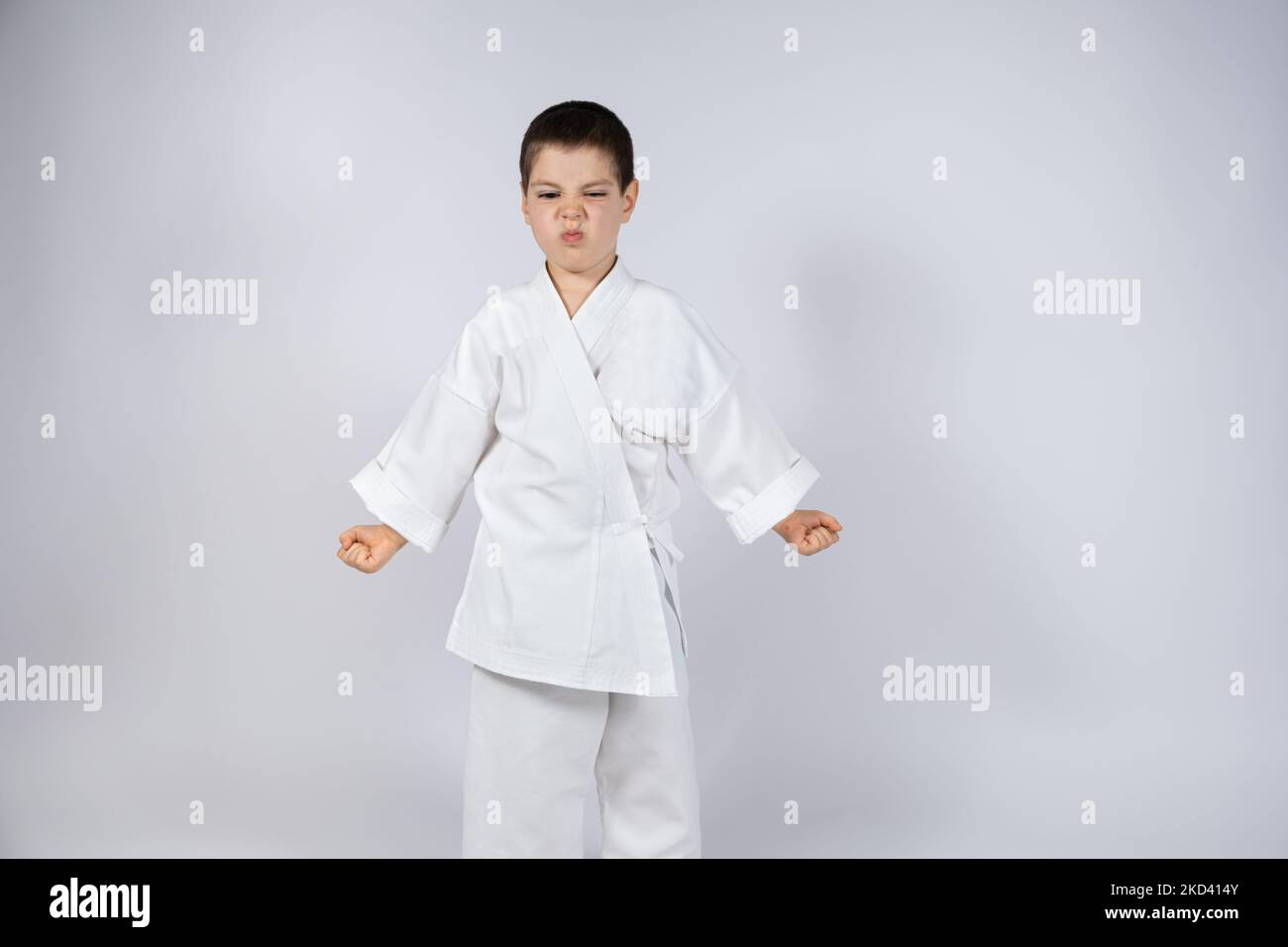 A 5yearold boy in a kimono practices karate on a white background