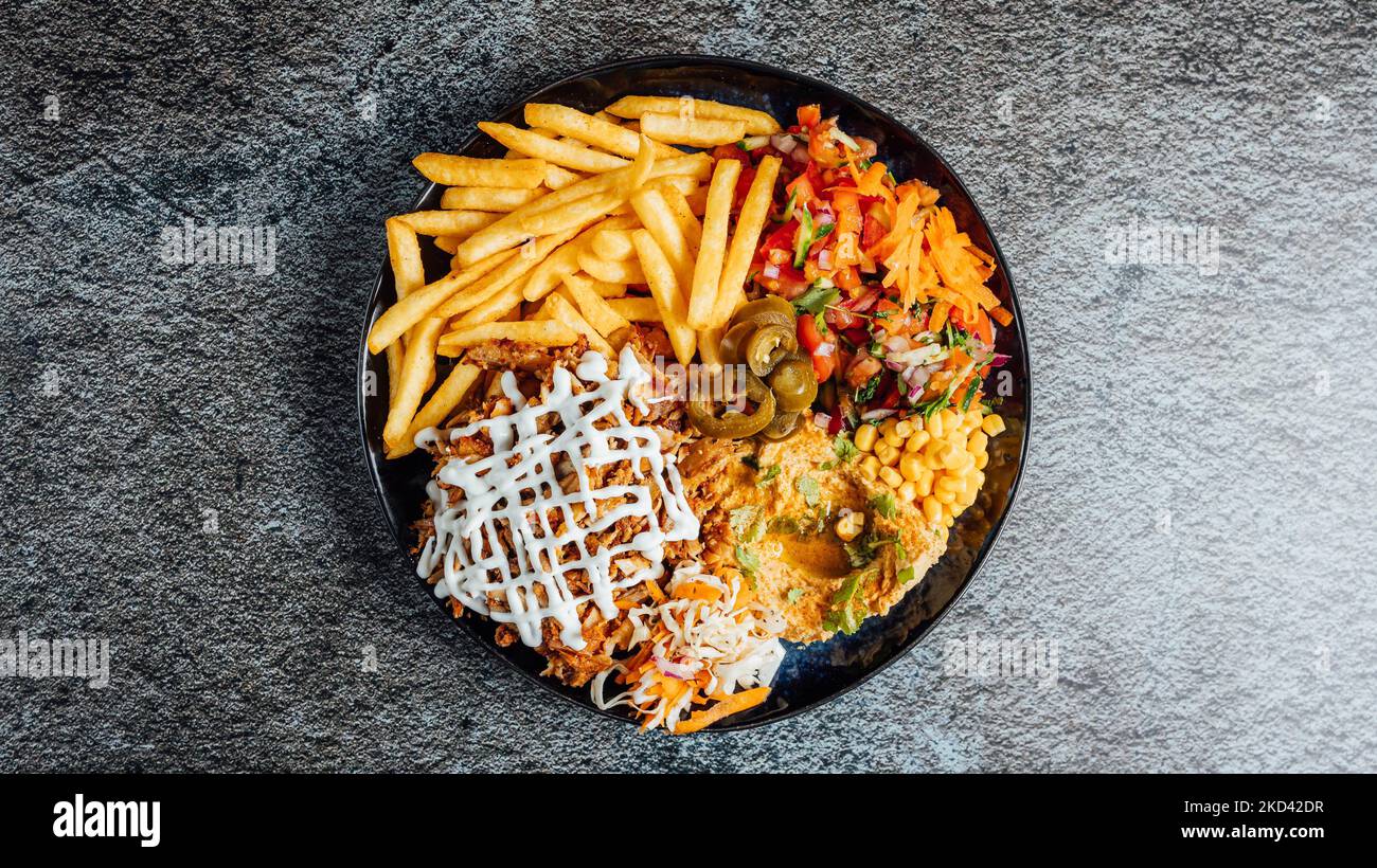 A top view of a mixed dish with fries, chicken, and veggies Stock Photo