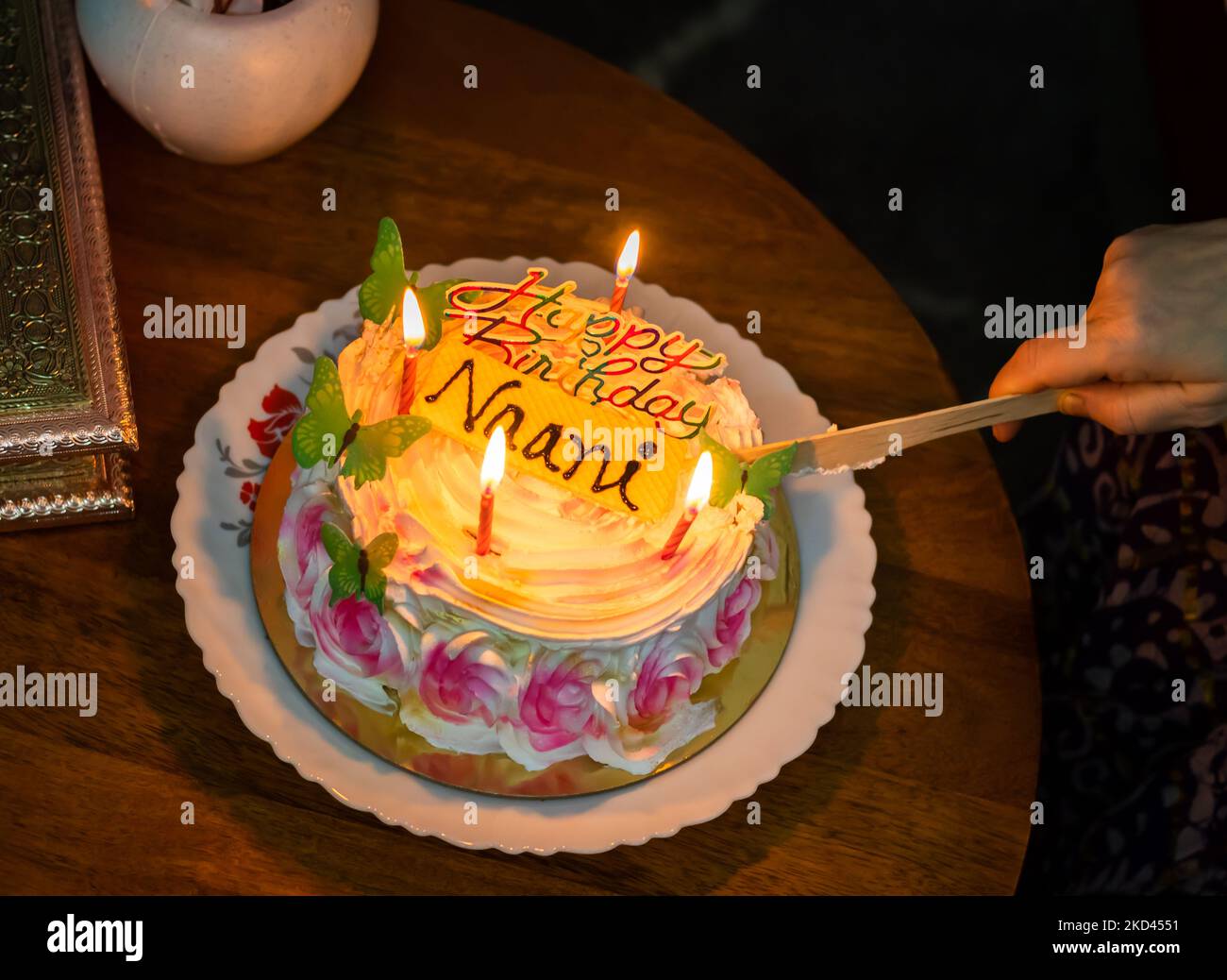 maternal grandmother cutting birthday cake decorated with lighted candles at coffee table Stock Photo