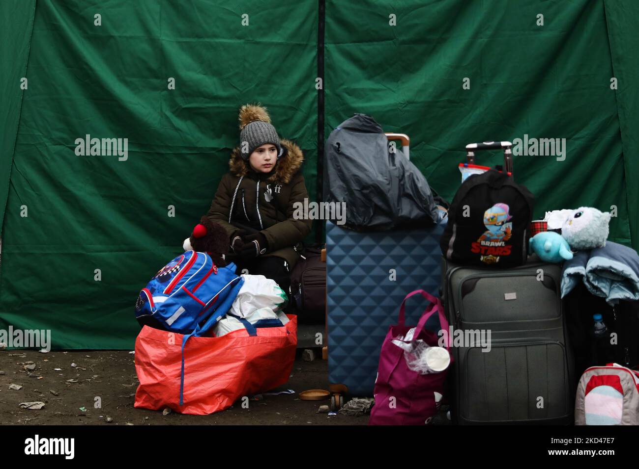A boy fleeing from Ukraine sits on a luggage after crossing the border