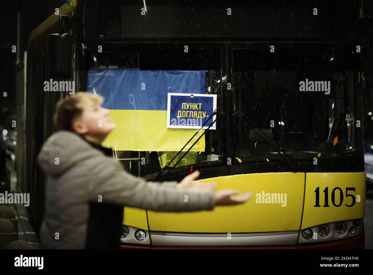 A man holds out his hands during a short hail storm in front of a bus with supplies for Ukrainian refugess and a Ukrainian flag at the Warsaw East train station in Warsaw, Poland on 04 March, 2022. Every day several thousand refugees arrive in Warsaw train stations, fleeing the violence after Russia's invasion. Nearly one million people have fled Ukraine after the Russian invasion and approximately 700 thousand of those have fled to Poland. Thanks to a number of private and public initiatives and the efforts of local municipalities refugees from Ukraine have been received with open arms and en Stock Photo