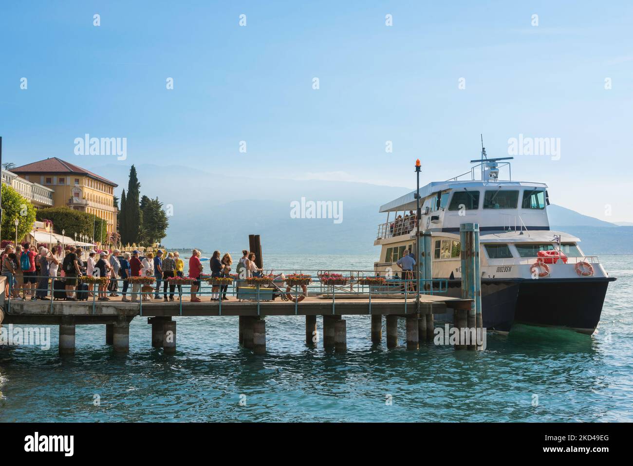 Ferry Lake Garda, view in summer of people standing on the ferry station jetty waiting to board a ferry boat in Gardone Riviera, Lombardy, Italy Stock Photo
