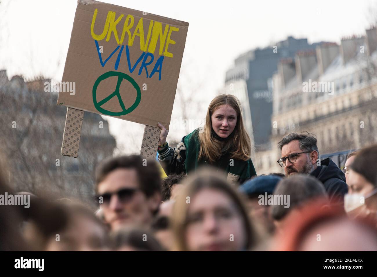 A young woman sitting on her friend's shoulders holds up a sign with a peace symbol in Ukrainian colors during the demonstration that brought together several thousand people who gathered in Paris to participate in a large march from the Place de la République to the Place de la Bastille to demand peace in Ukraine on the 10th day of the invasion of Russia. Many political figures and ordinary citizens marched amidst Ukrainian flags and slogans for peace and against Putin, in Paris on March 5, 2022. (Photo by Samuel Boivin/NurPhoto) Stock Photo